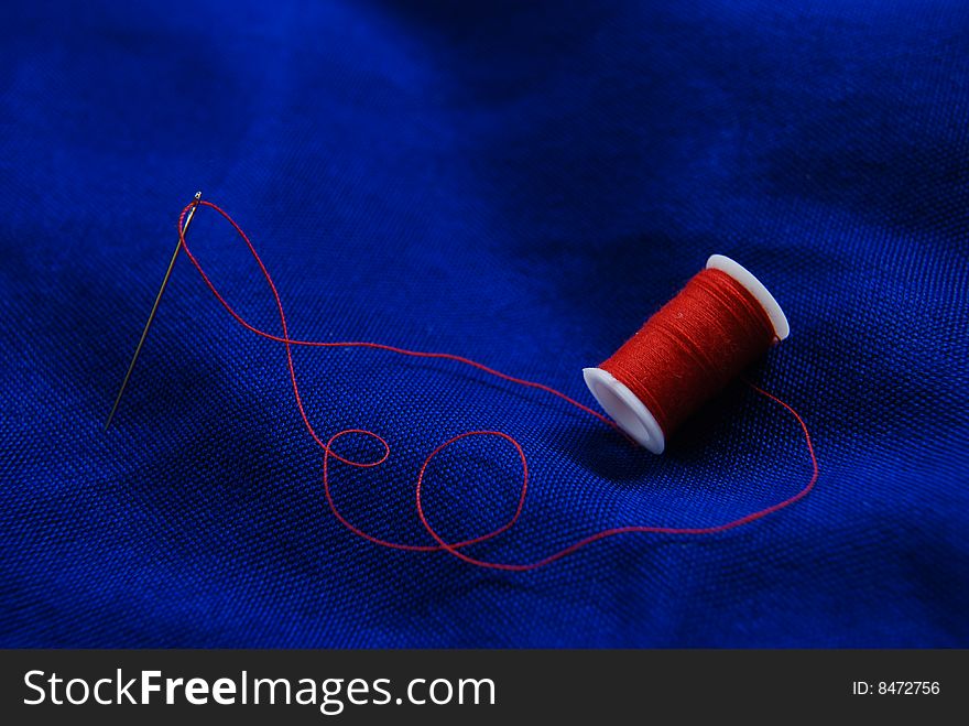 Needle and red thread on blue background. Needle and red thread on blue background