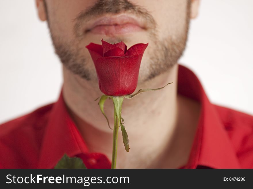 A man, holding a beautiful red rose in front of his face, wearing a red shirt. A man, holding a beautiful red rose in front of his face, wearing a red shirt