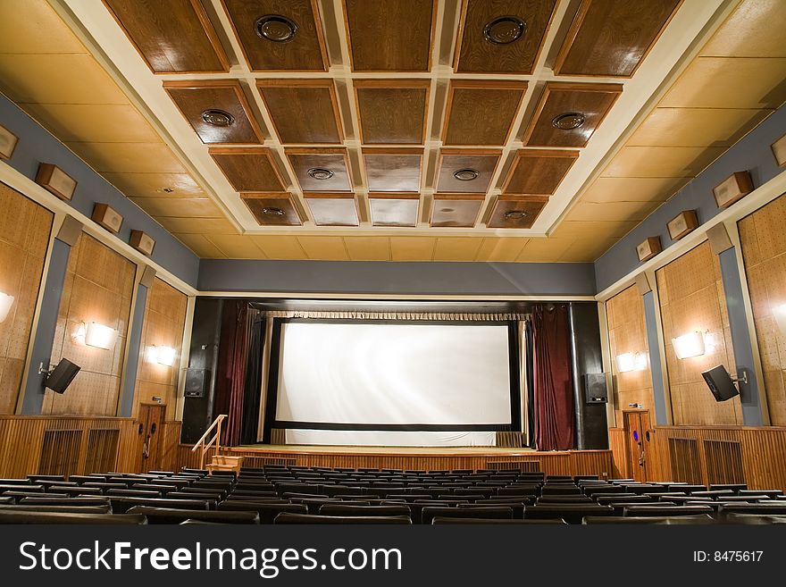 Empty old retro style cinema auditorium with line of chairs and stage with silver screen. Ready for adding your own picture. Empty old retro style cinema auditorium with line of chairs and stage with silver screen. Ready for adding your own picture.