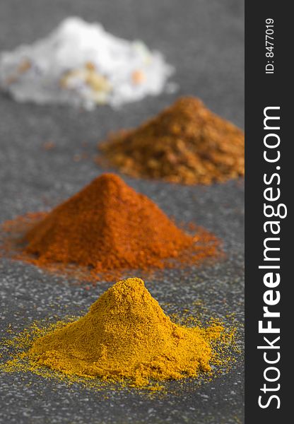 Four colorful piles of ground spices on grey background. Four colorful piles of ground spices on grey background