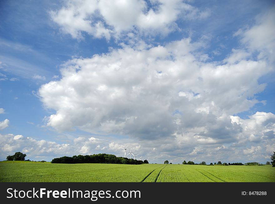 Landscape with green field and cloudscape. In the background you can see five wind turbines. Landscape with green field and cloudscape. In the background you can see five wind turbines.