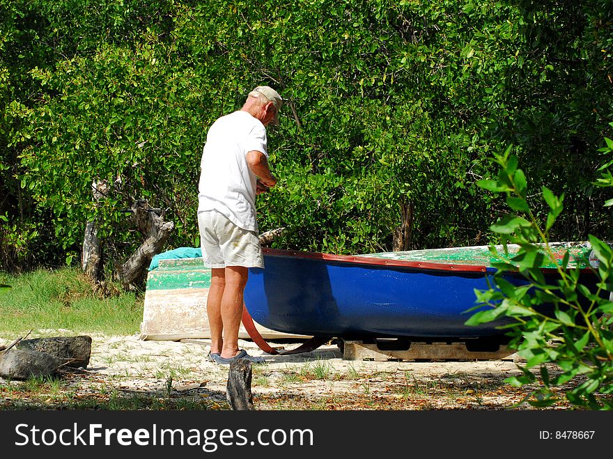 Senior man repairing small blue boat on island beach. Senior man repairing small blue boat on island beach.