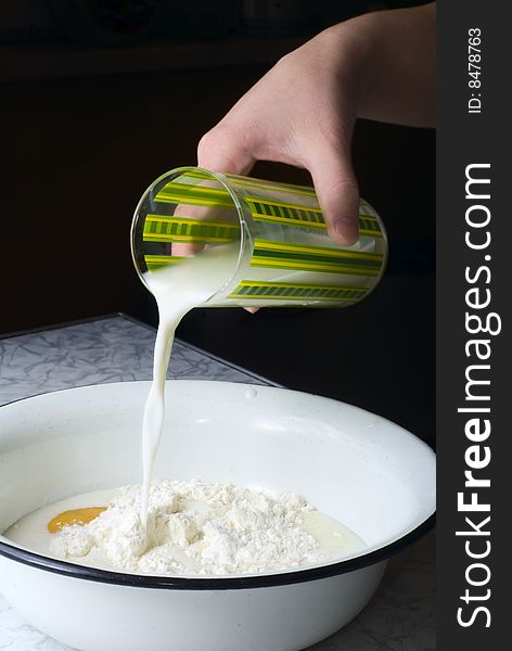 Woman pouring milk in the bowl with flour and egg in it. Woman pouring milk in the bowl with flour and egg in it