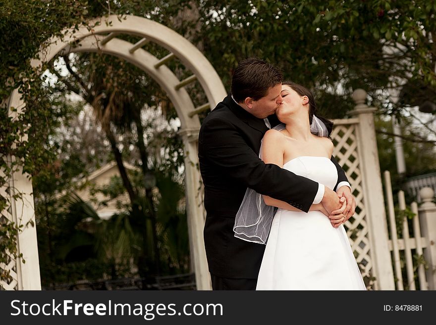 Newlyweds kissing in garden with arbor in background. Newlyweds kissing in garden with arbor in background