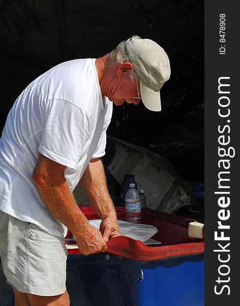 Senior man repairing small blue boat on island beach. Senior man repairing small blue boat on island beach.