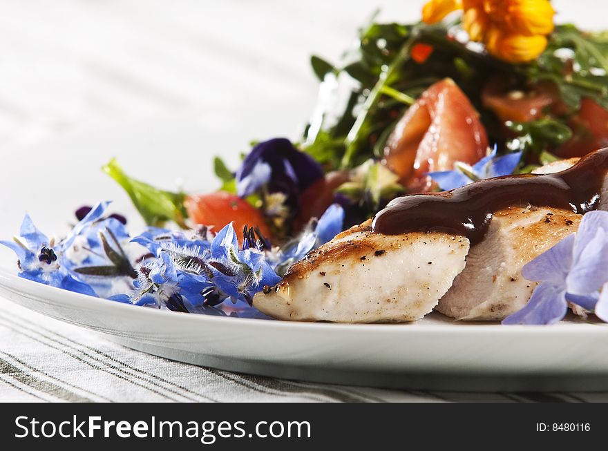 Grilled chicken breast served with salad and garnished with edible flowers