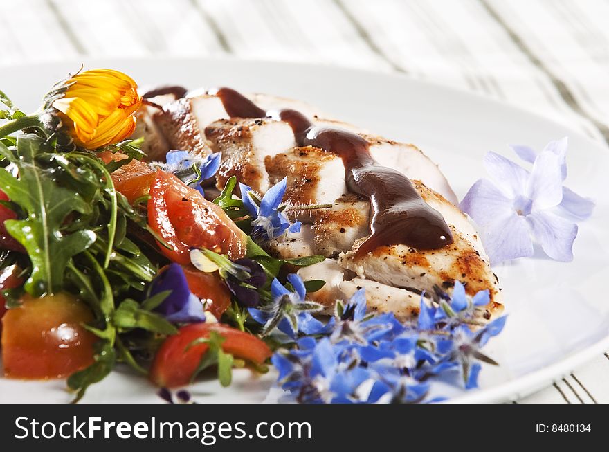 Grilled chicken breast served with salad and garnished with edible flowers