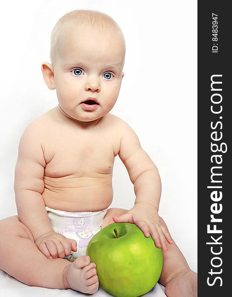 Beatiful baby boy is sitting and holding a very big apple. Background is white. Beatiful baby boy is sitting and holding a very big apple. Background is white.