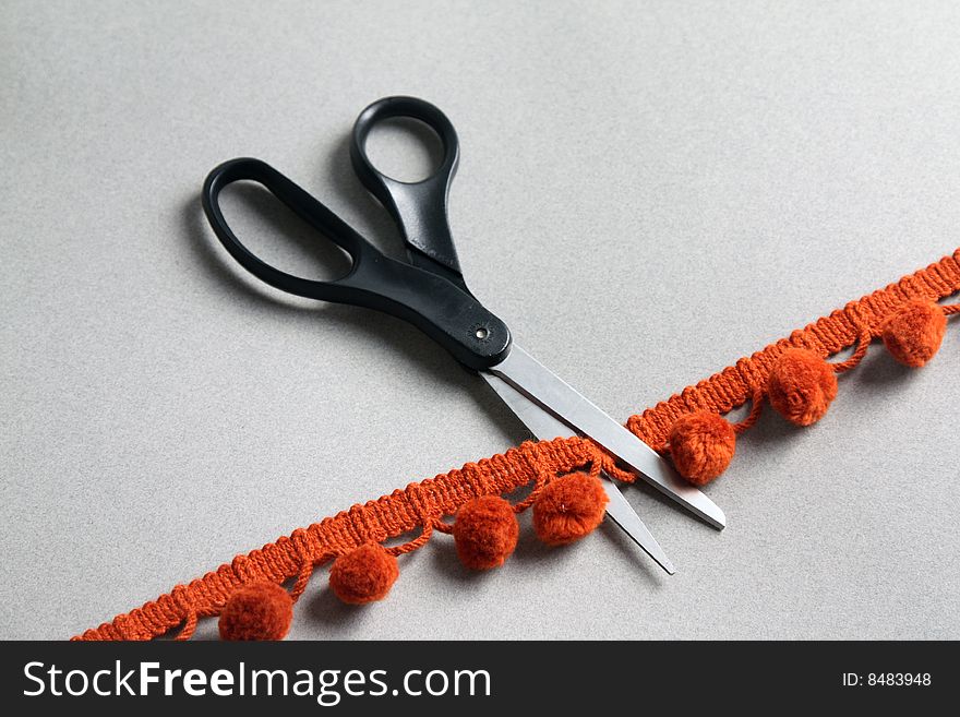 Scissors cutting through trim with pom poms. Scissors cutting through trim with pom poms