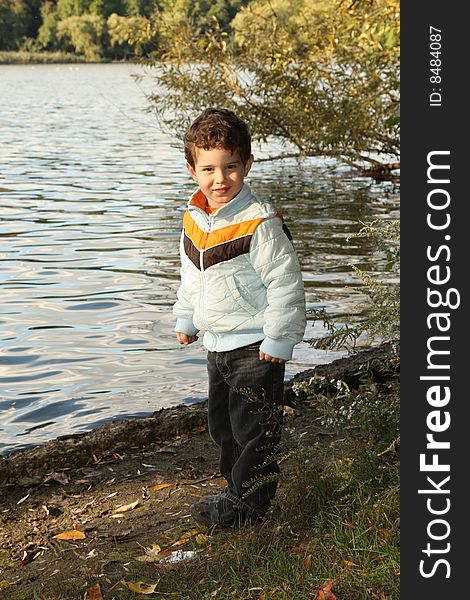 Young cute boy standing by the lake at a park. Young cute boy standing by the lake at a park