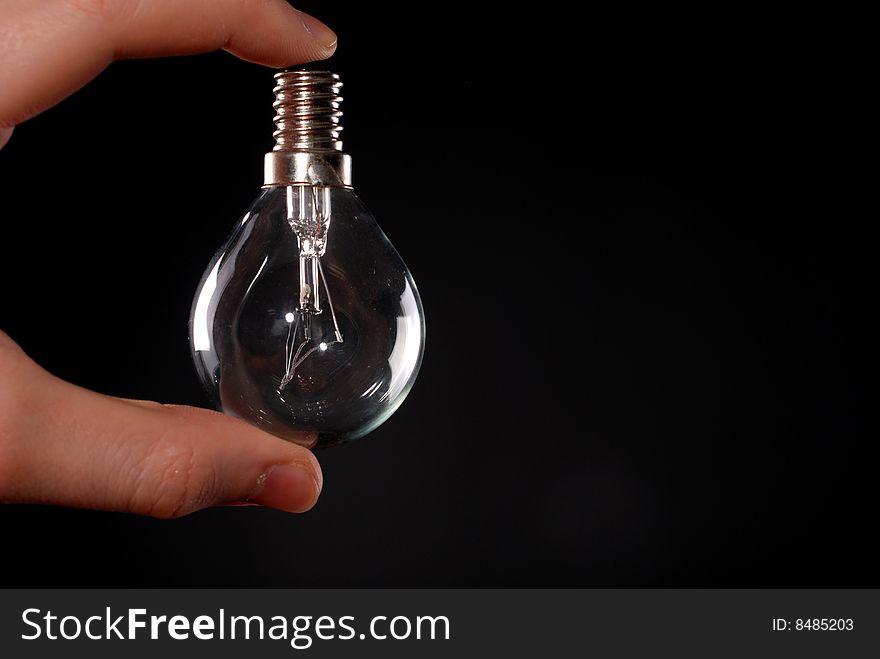 Electric lamp in male fingers at black background