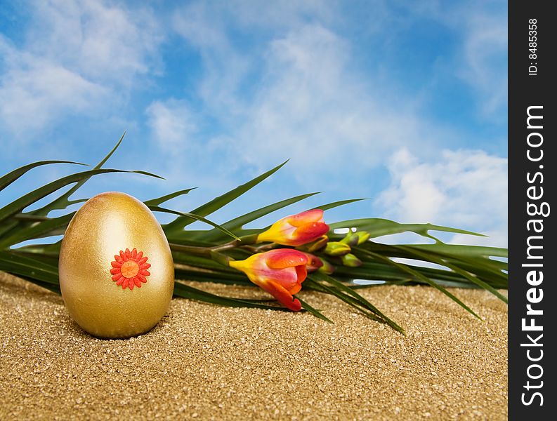 Celebrating Easter with golden decorated egg and spring freesia flowers over blue sky with room for your text. Celebrating Easter with golden decorated egg and spring freesia flowers over blue sky with room for your text.
