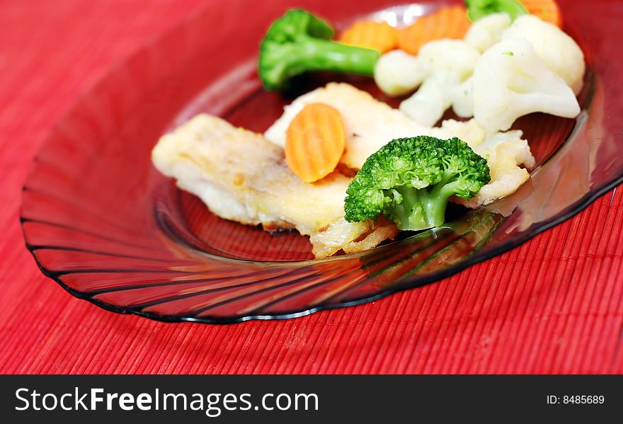 Plate with fish and vegetables on red table. Plate with fish and vegetables on red table