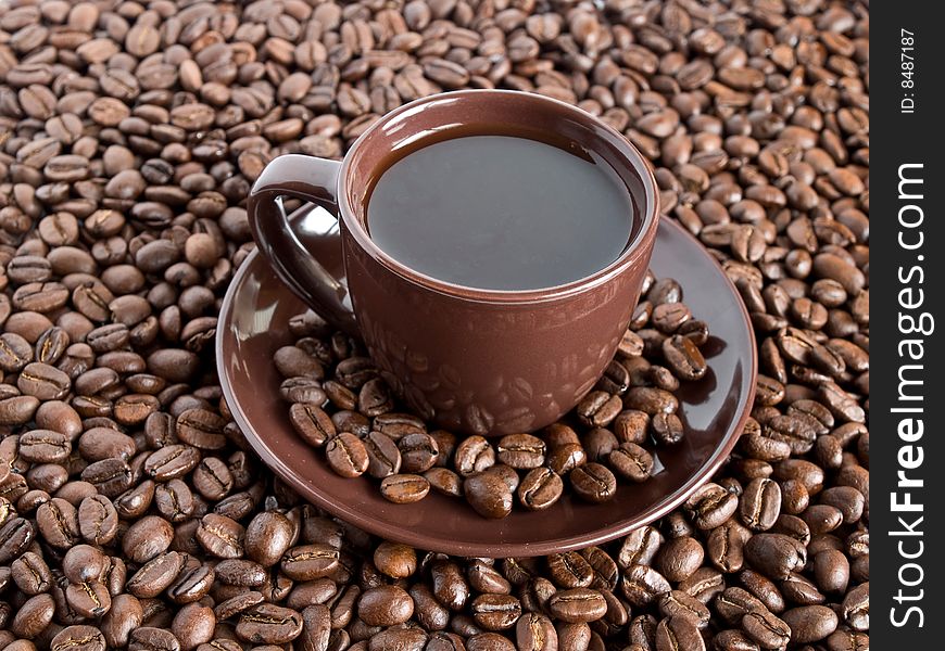 A close-up composition of a cup of coffee with saucer and being surrounded with coffee beans. A close-up composition of a cup of coffee with saucer and being surrounded with coffee beans