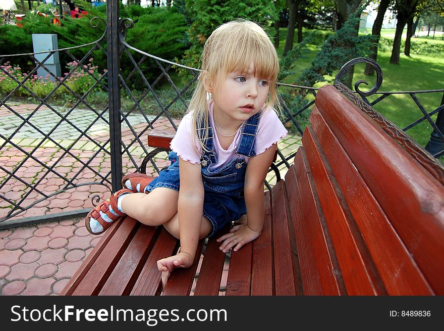 Little melancholy girl sit cross-legged in park on bench