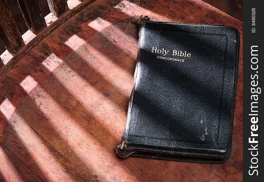 A black leather bible sits on an old wooden chair with rays of sunlight beaming through. A black leather bible sits on an old wooden chair with rays of sunlight beaming through.