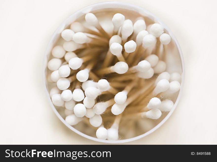 A close up on a container full of cotton swabs on a white background.
