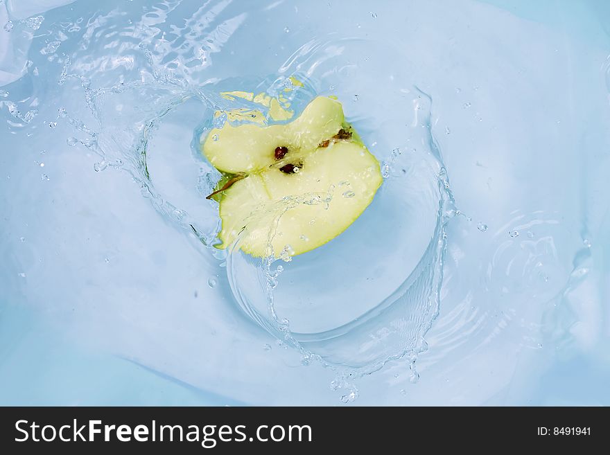 Green apple falling into blue water