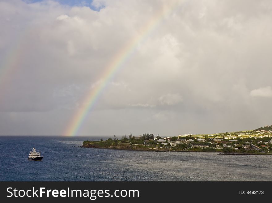 A ferry cruising past an island with a rainbow in the cloudy sky. A ferry cruising past an island with a rainbow in the cloudy sky