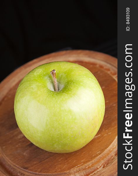 Granny smith green apple on a wooden platter against a black background. Granny smith green apple on a wooden platter against a black background