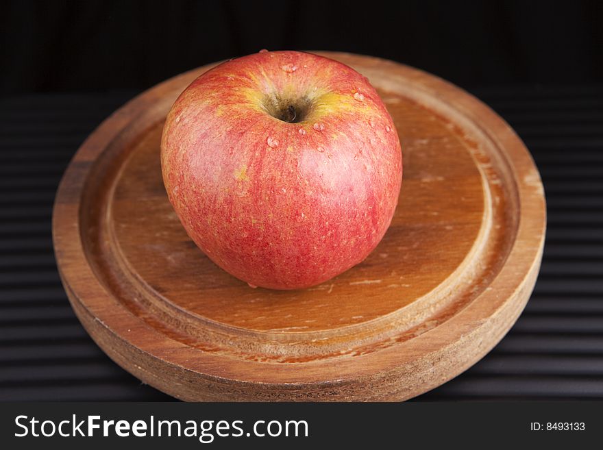 A red apple on a wooden serving platter against a black background. A red apple on a wooden serving platter against a black background.