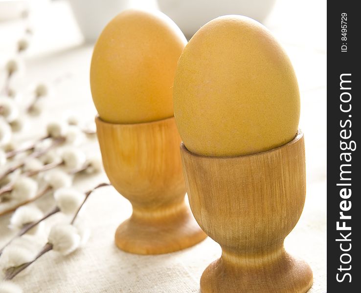 Yellow easter eggs in wooden cups and some catkins on table cloth