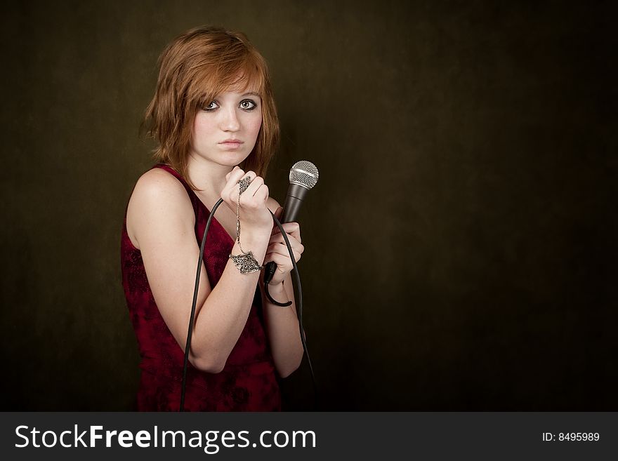 Pretty young girl with red hair on a green background with microphone. Pretty young girl with red hair on a green background with microphone