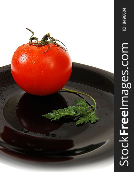 Wet red tomato with parsley on the black table. White bacjground. Drops on the tomato. Wet red tomato with parsley on the black table. White bacjground. Drops on the tomato.