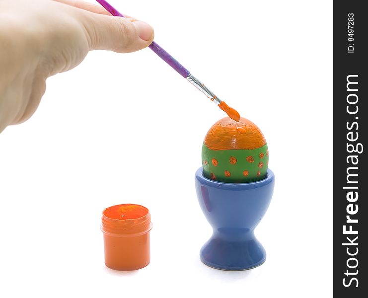 Egg in the blue stand and a hand holding the brush with the orange paint
