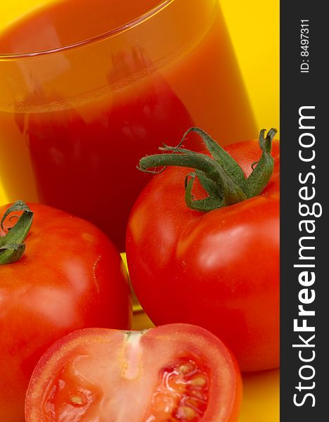 Ripe juicy tomatoes and glass of tomato juice on a yellow background. Ripe juicy tomatoes and glass of tomato juice on a yellow background