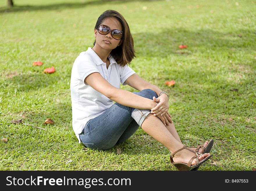 A female sitting down resting and enjoying the park under a tree shade. A female sitting down resting and enjoying the park under a tree shade