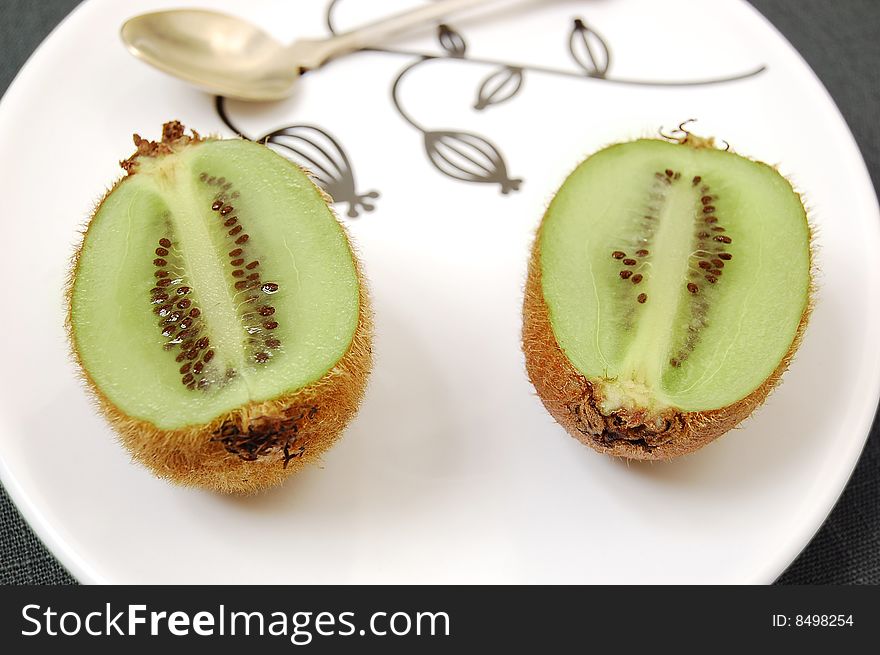 Two half kiwifruit on the white dessert-plate view from above.