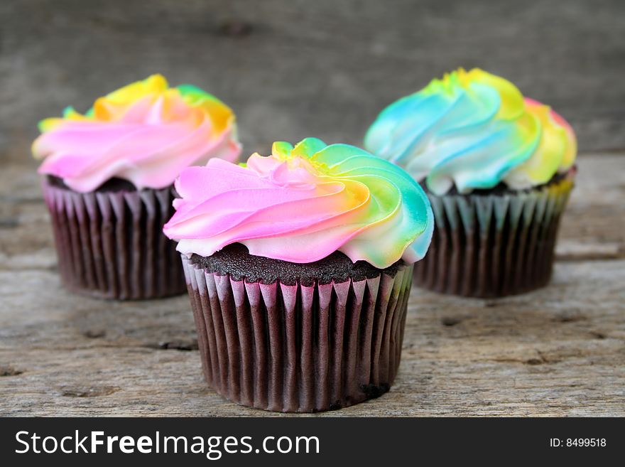 Chocolate cupcakes with multi colored icing shot on a rustic background.