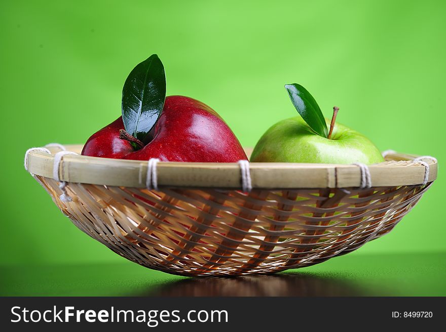 Green and red apples in basket, green background