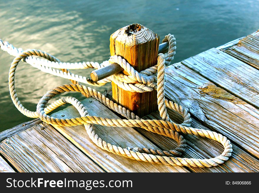 Boat (not shown) moored to post on wooden jetty with spare rope twisted loosely around. Boat (not shown) moored to post on wooden jetty with spare rope twisted loosely around.