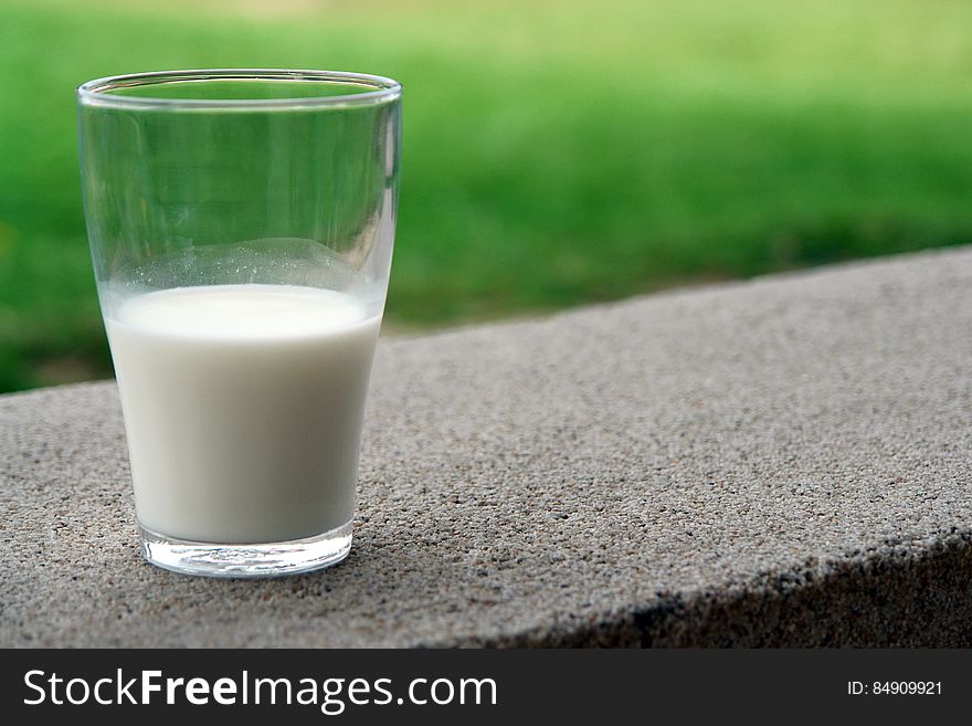 A close up of a glass of milk on a concrete surface outdoor.