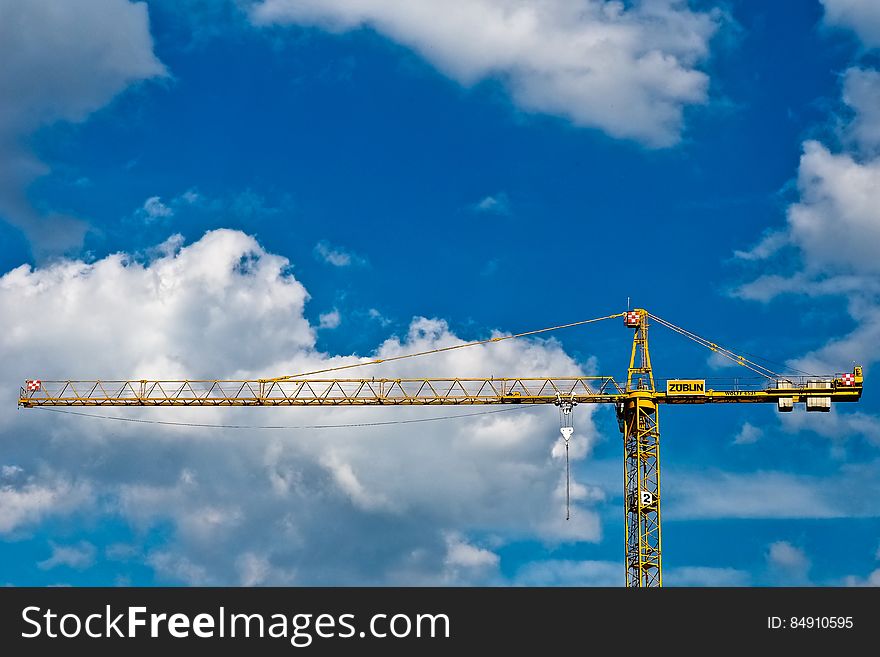 Upper parts of computerized crane with supporting cables and main steel column seen against blue sky and fluffy white clouds. Upper parts of computerized crane with supporting cables and main steel column seen against blue sky and fluffy white clouds.