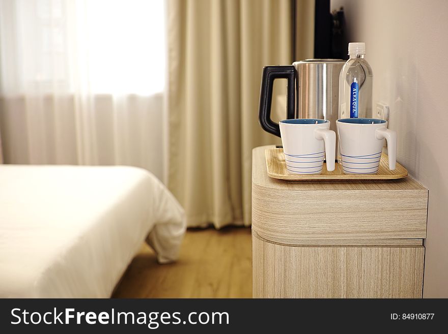 A hotel or guest room with a water kettle, cups and other items on the bedside table. A hotel or guest room with a water kettle, cups and other items on the bedside table.