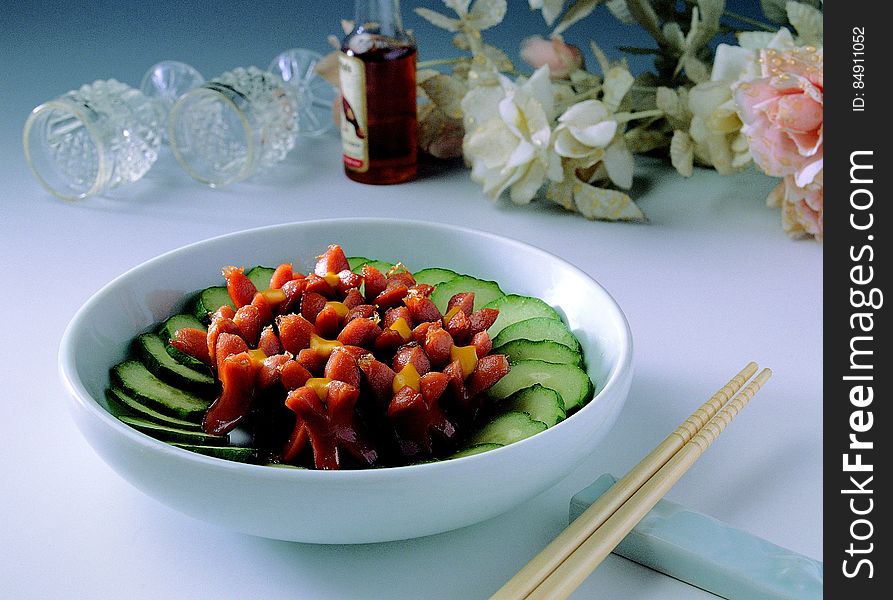A bowl of salad on table with chopsticks and floral arrangement. A bowl of salad on table with chopsticks and floral arrangement.