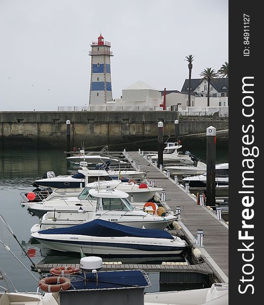 Lighthouse on seawall with boats along dock on waterfront. Lighthouse on seawall with boats along dock on waterfront.