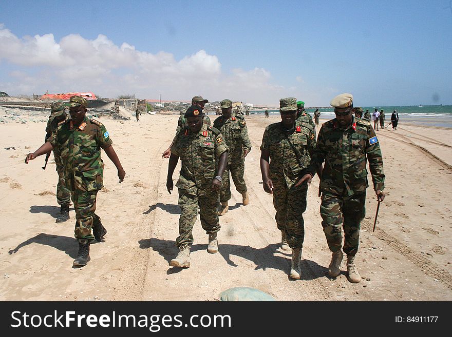 Soldiers in uniform walking on sandy beach on sunny day. Soldiers in uniform walking on sandy beach on sunny day.