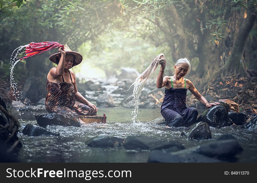A couple of Asian women washing clothes in the river.