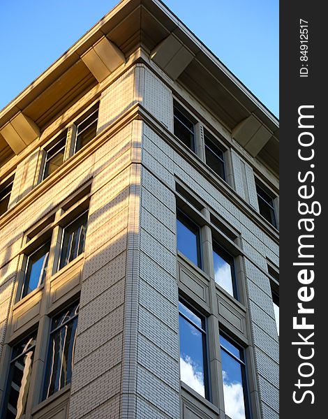 Corner of modern architect designed office building constructed of gray brick and glass with eaves and soffit visible, blue sky and cloud reflected in the glass. Corner of modern architect designed office building constructed of gray brick and glass with eaves and soffit visible, blue sky and cloud reflected in the glass.