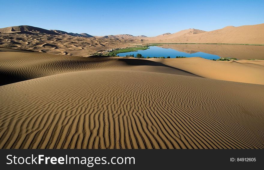 Landscape of ridged desert sands and blue lake dunes extending into the far distance, cloudless blue sky background. Landscape of ridged desert sands and blue lake dunes extending into the far distance, cloudless blue sky background.