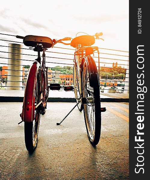 Two bicycles parked side by side in city with bright sun flare. Two bicycles parked side by side in city with bright sun flare.