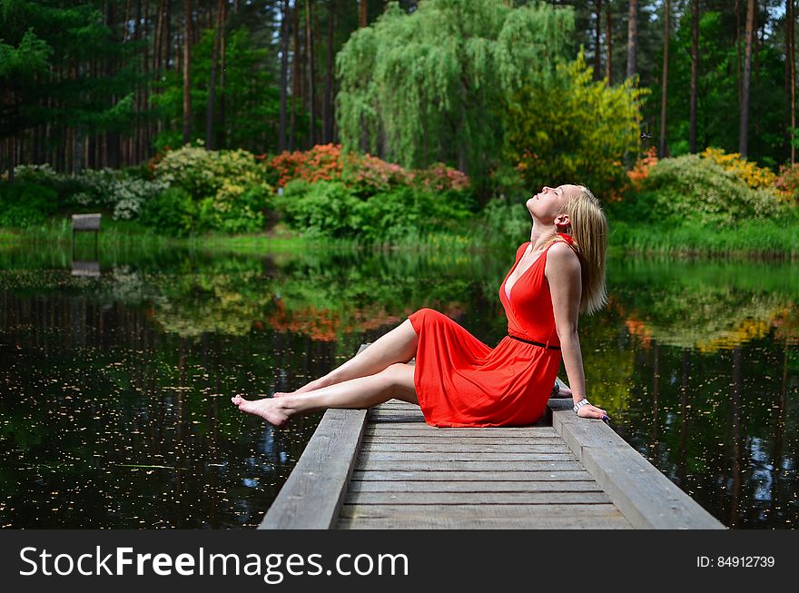 Beautiful woman in red dress sat on pier relaxing by lake in countryside. Beautiful woman in red dress sat on pier relaxing by lake in countryside.