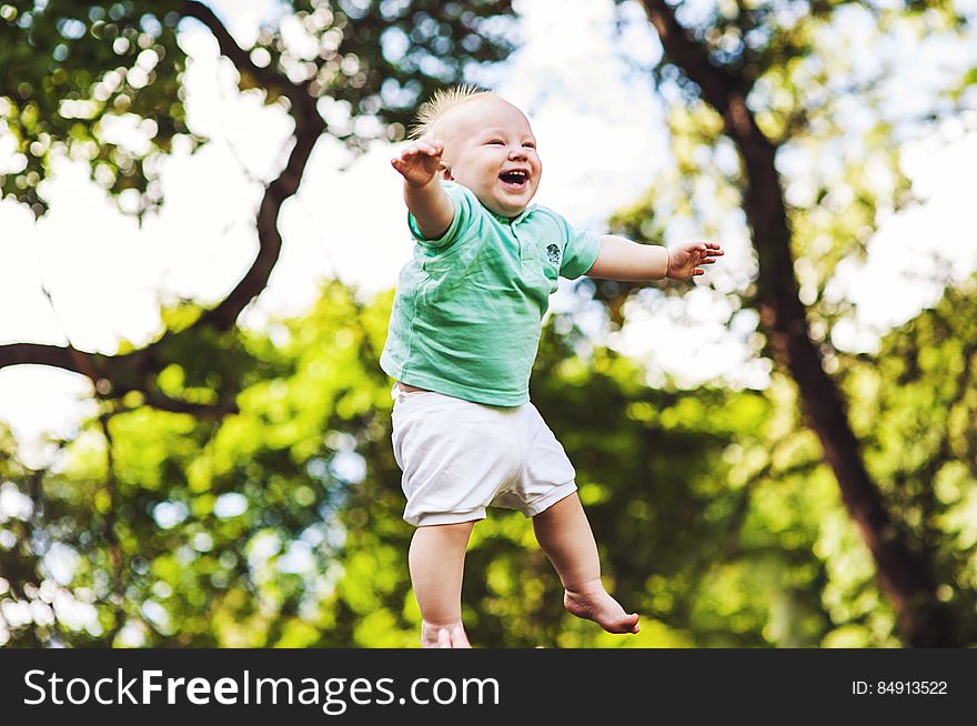 Happy young baby boy jumping in midair with trees in background.