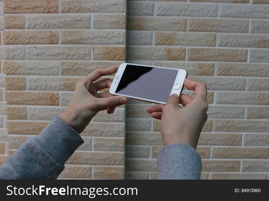 Two adult hands holding a smart phone against a brick background. Two adult hands holding a smart phone against a brick background.
