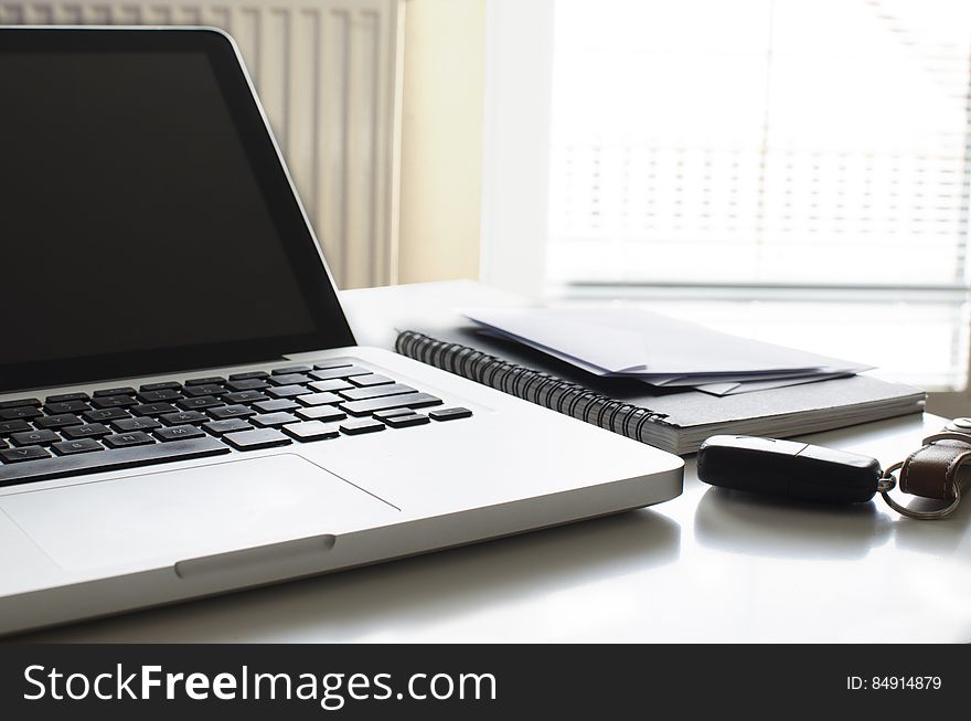 Laptop computer on desk showing keyboard and screen with spiral notebook along side, office background. Laptop computer on desk showing keyboard and screen with spiral notebook along side, office background.