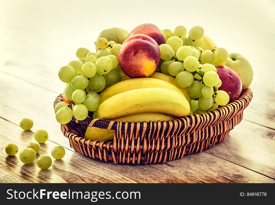 Bowl of fresh fruit with grapes, apple and bananas on wooden table.